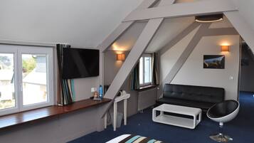 A modern loft bedroom with a large window, a flat-screen TV, a black leather sofa, a white coffee table, and a unique egg chair.