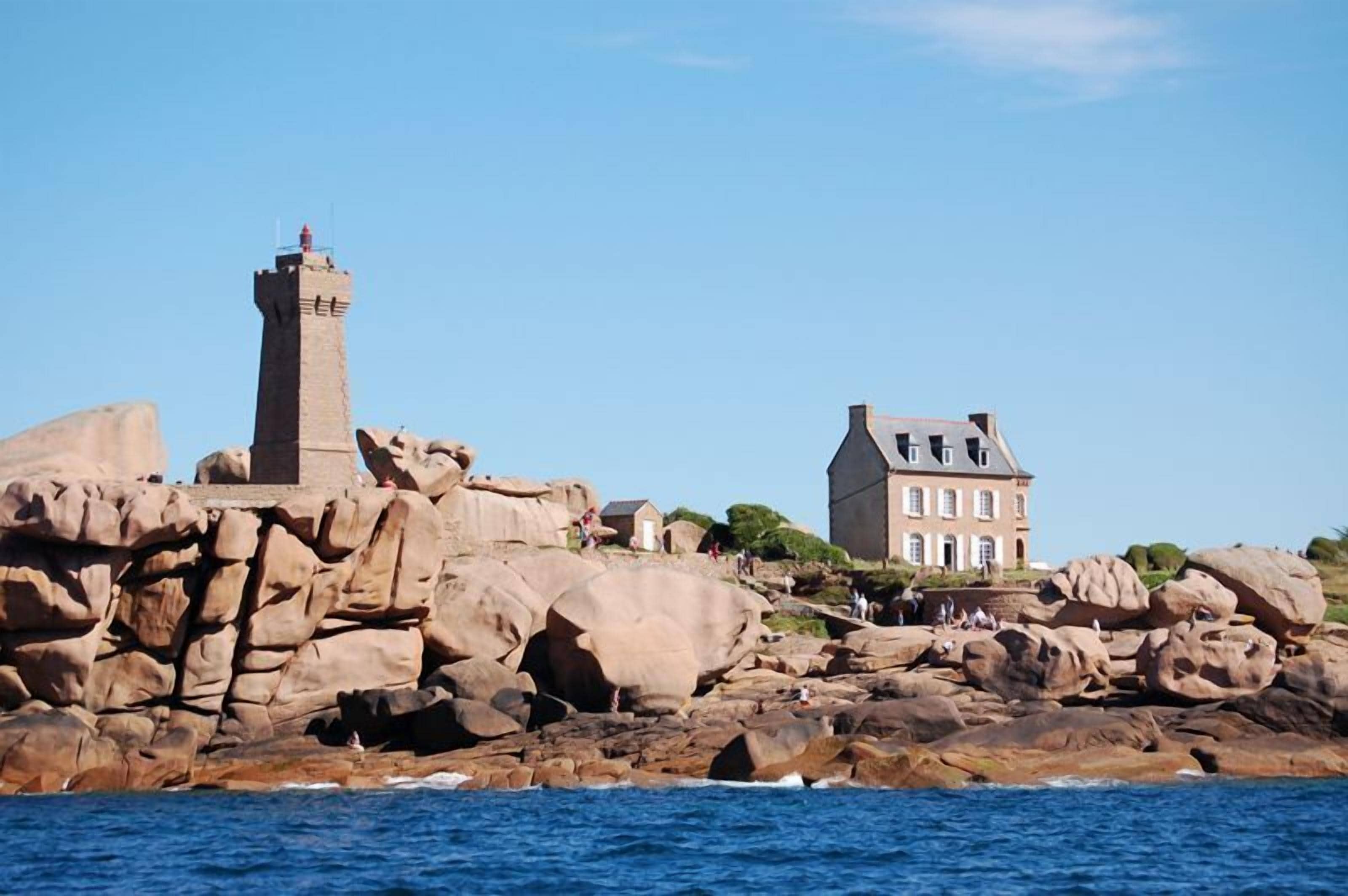 A coastal scene with a lighthouse and a large house on rocky terrain.