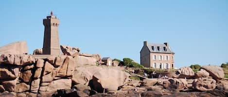 A coastal scene with a lighthouse and a large house on rocky terrain.