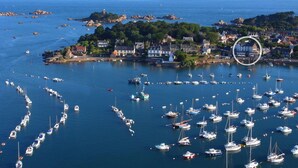 Un pueblo costero con un puerto deportivo lleno de barcos, casas y afloramientos rocosos.