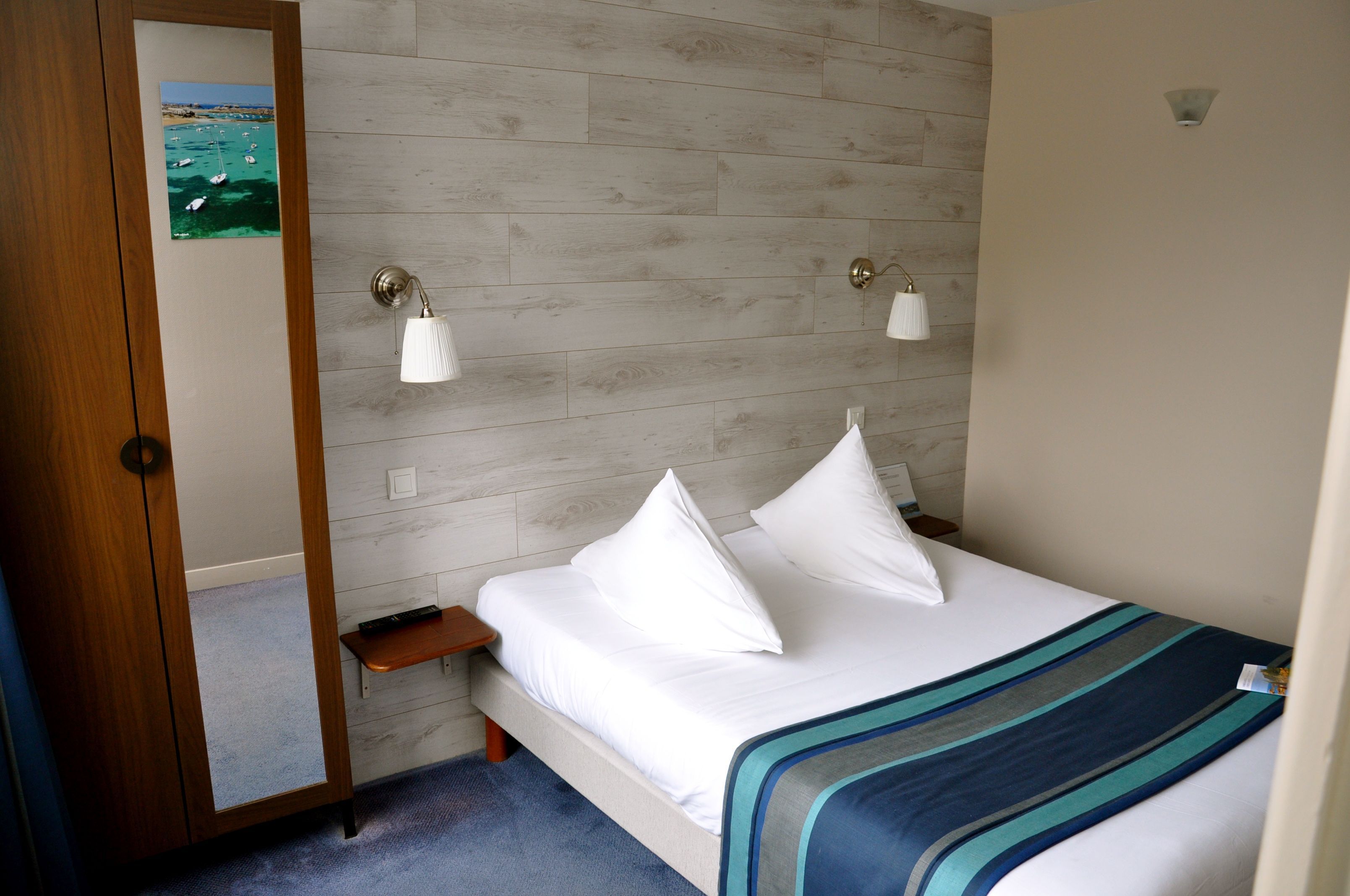 Habitación de hotel con pared de madera, cama con ropa blanca, dos lámparas de noche y una mesita de noche de madera.