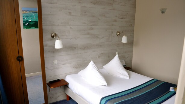 Habitación de hotel con pared de madera, cama con ropa blanca, dos lámparas de noche y una mesita de noche de madera.