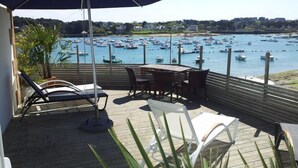 A deck with a view of a marina filled with boats, a table, chairs, and a large umbrella providing shade. - Hôtel des Rochers (Perros-Guirec)