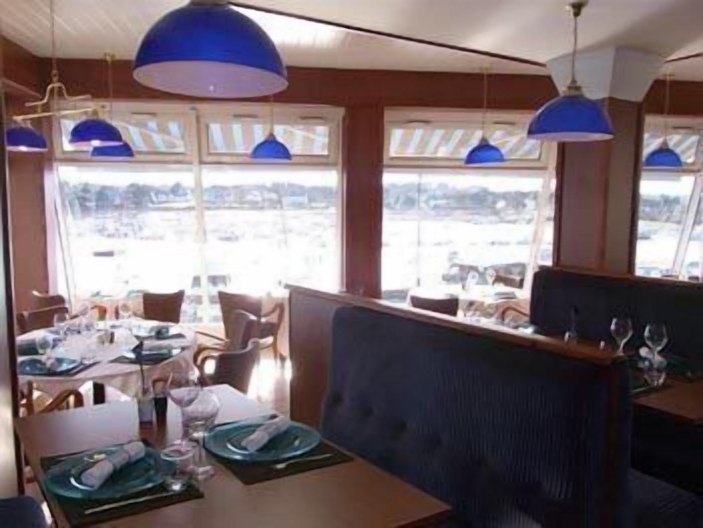 A dining area with tables set for a meal, large windows with a view, and blue pendant lighting.