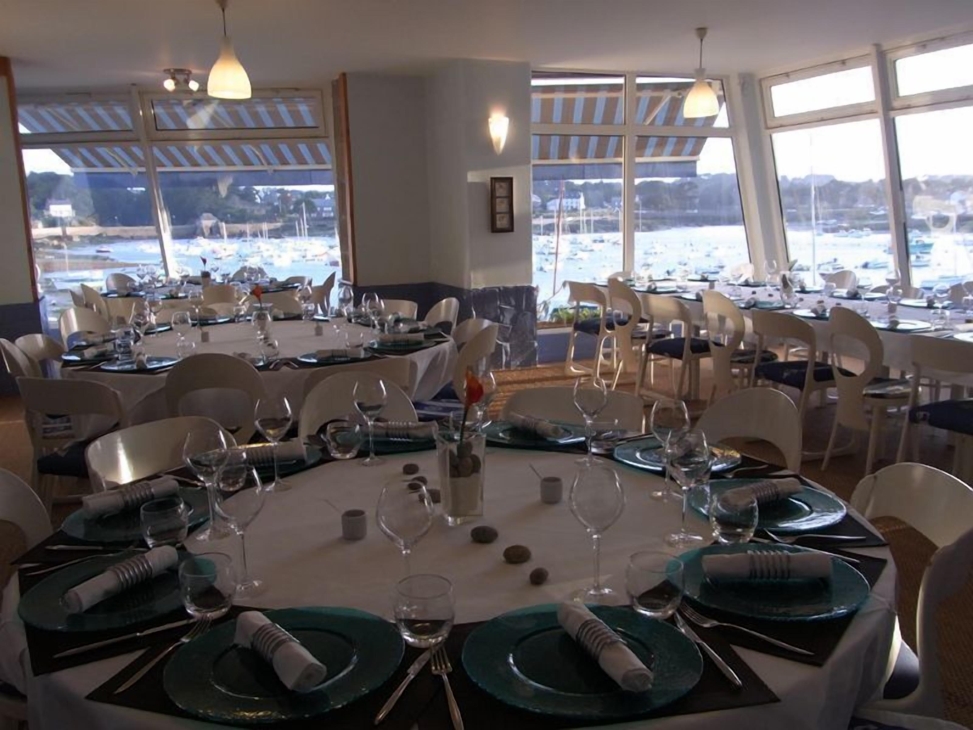A dining area with round tables set for a meal, large windows with a view of a marina, and a ceiling with a striped pattern.