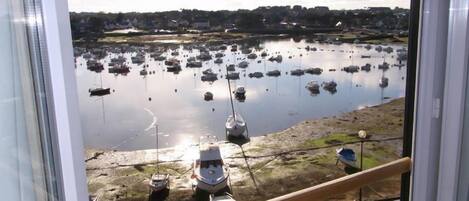 Vista de uma marina com vários barcos atracados, uma orla arenosa e uma linha costeira distante com edifícios.
