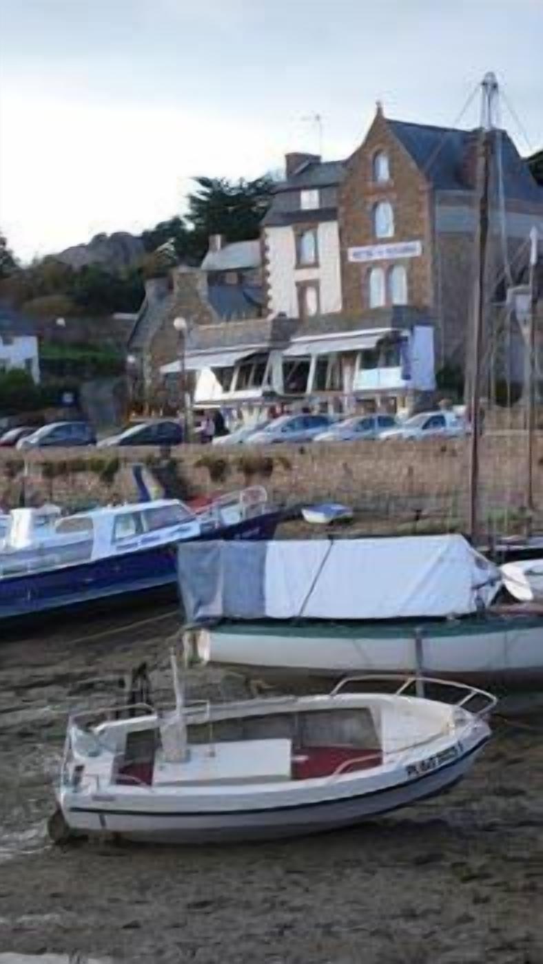 A marina with several boats docked, a building with a sign in the background, and a hill with trees.