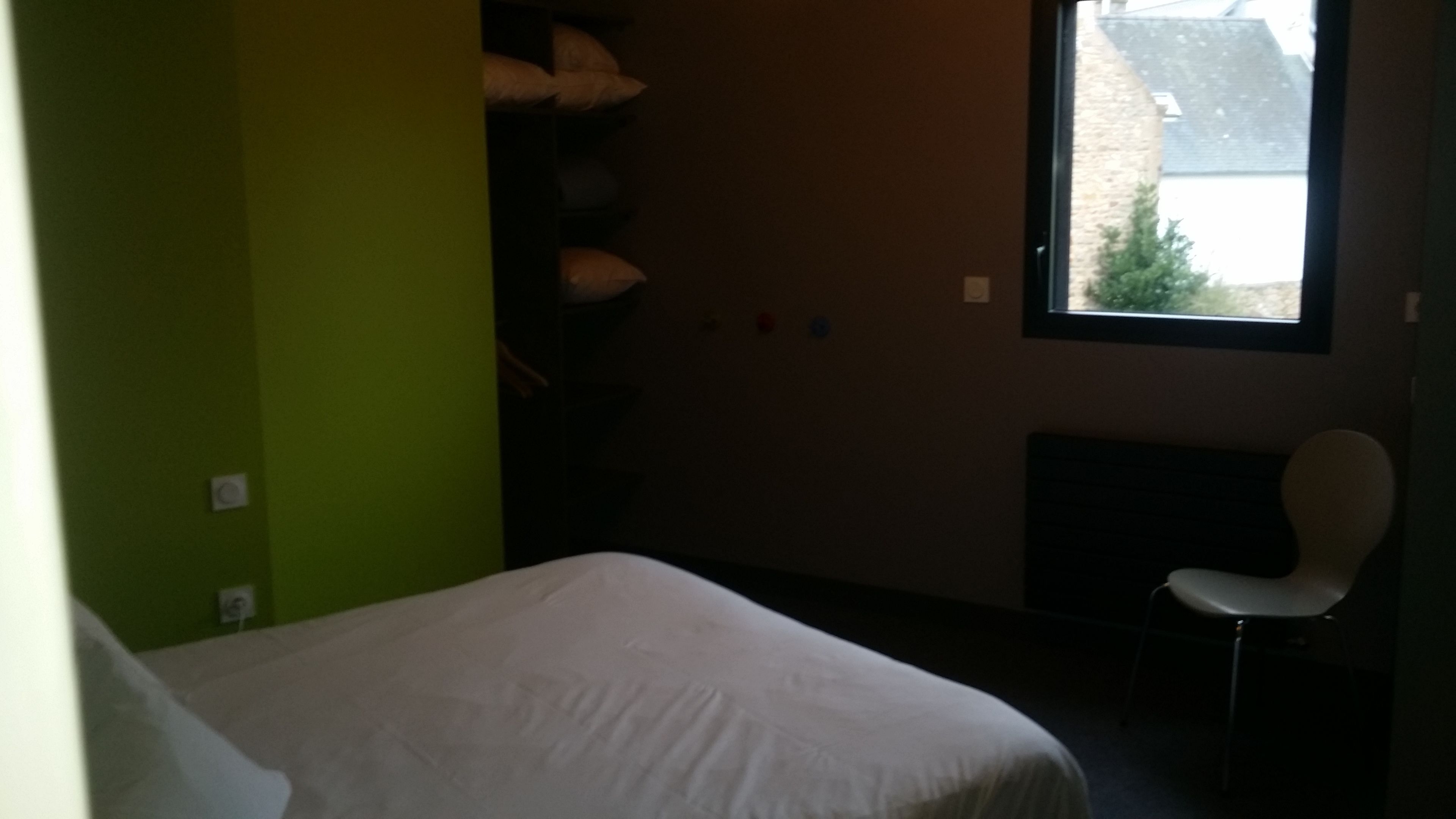 Une pièce avec un lit, une chaise, une fenêtre et un mur vert.