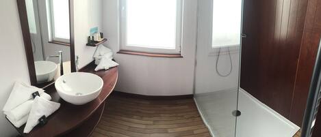 A modern bathroom with a large sink, a mirror, a shower, and a wooden floor.