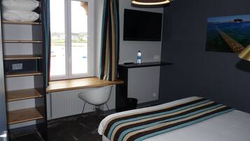 A hotel room with a bed, a desk with a chair, a TV, a window with curtains, and a painting on the wall.