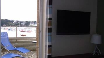 A room with a view of a marina, a blue chair, a white lamp, and a black screen on the wall.