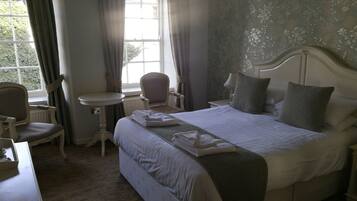 A neatly arranged bedroom with a large bed, a small table, a chair, and a window with curtains.