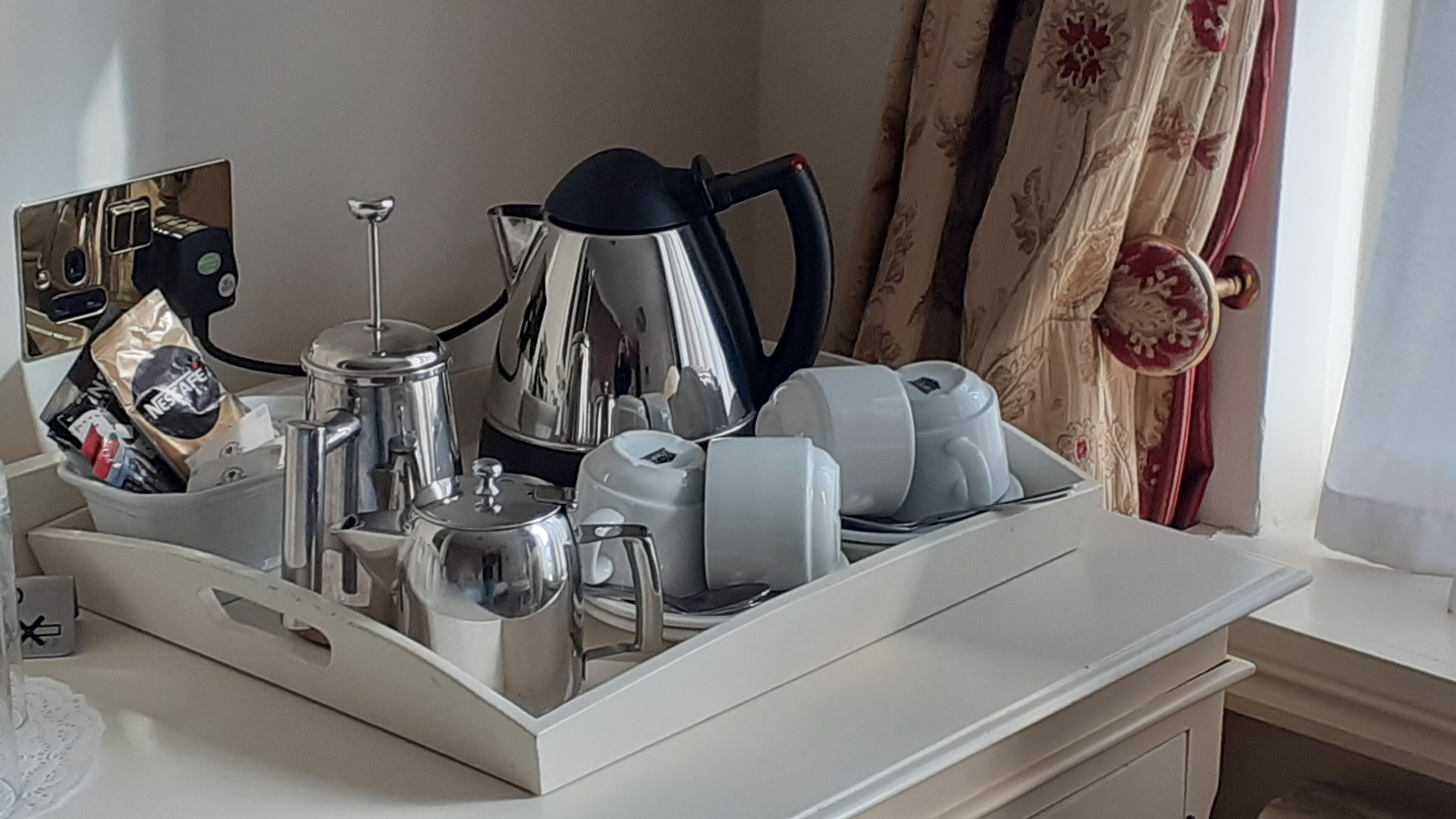 A kitchen area with a coffee maker, kettle, and cups on a countertop.