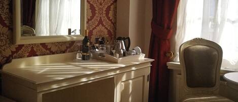 A hotel room with a large white vanity, a mirror, a chair, and a window with curtains.