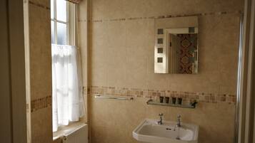 A bathroom with beige tiles, a window with a curtain, a sink, and a mirror.