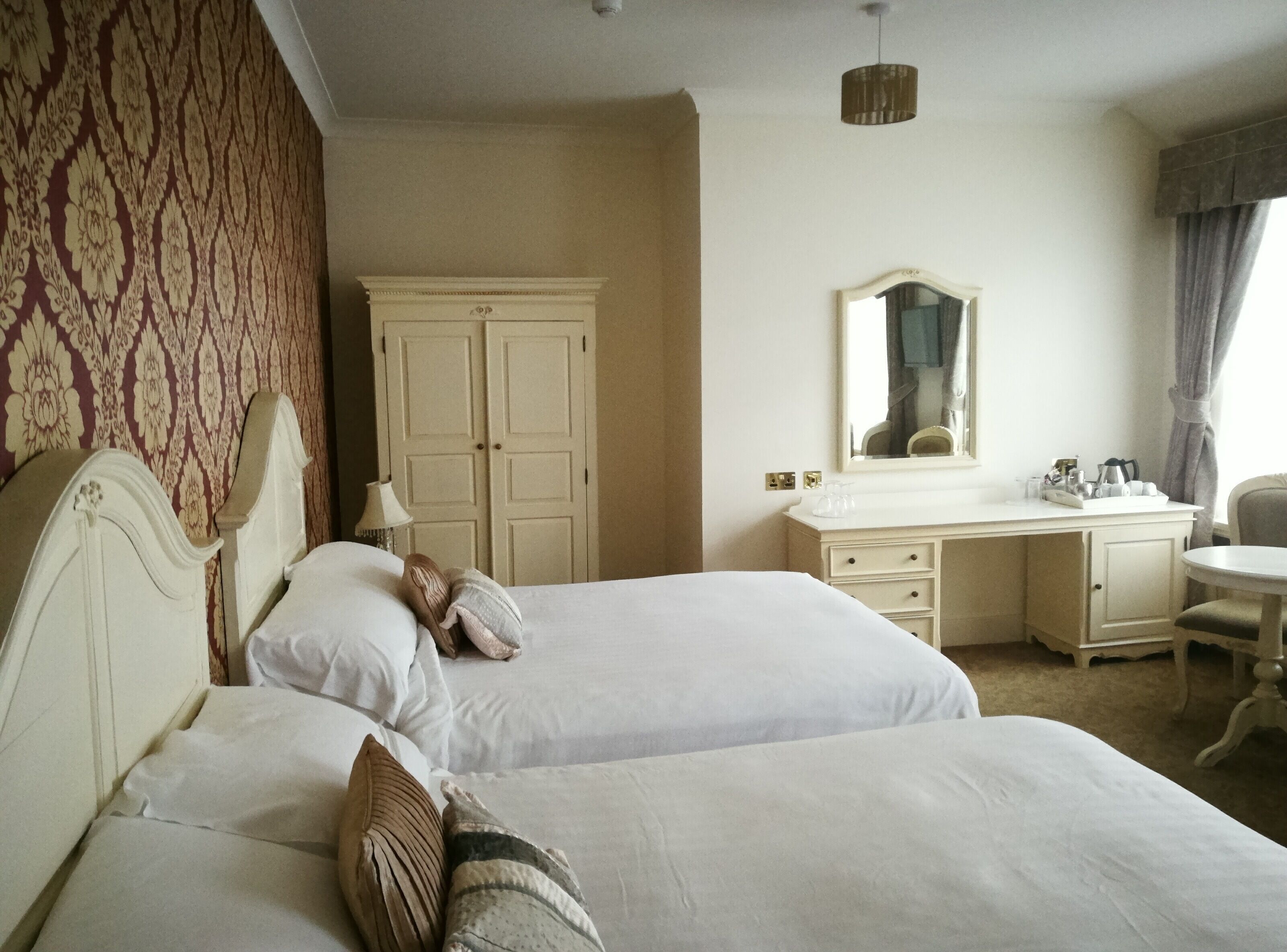 A hotel room with two beds, a dresser, a mirror, and a desk.