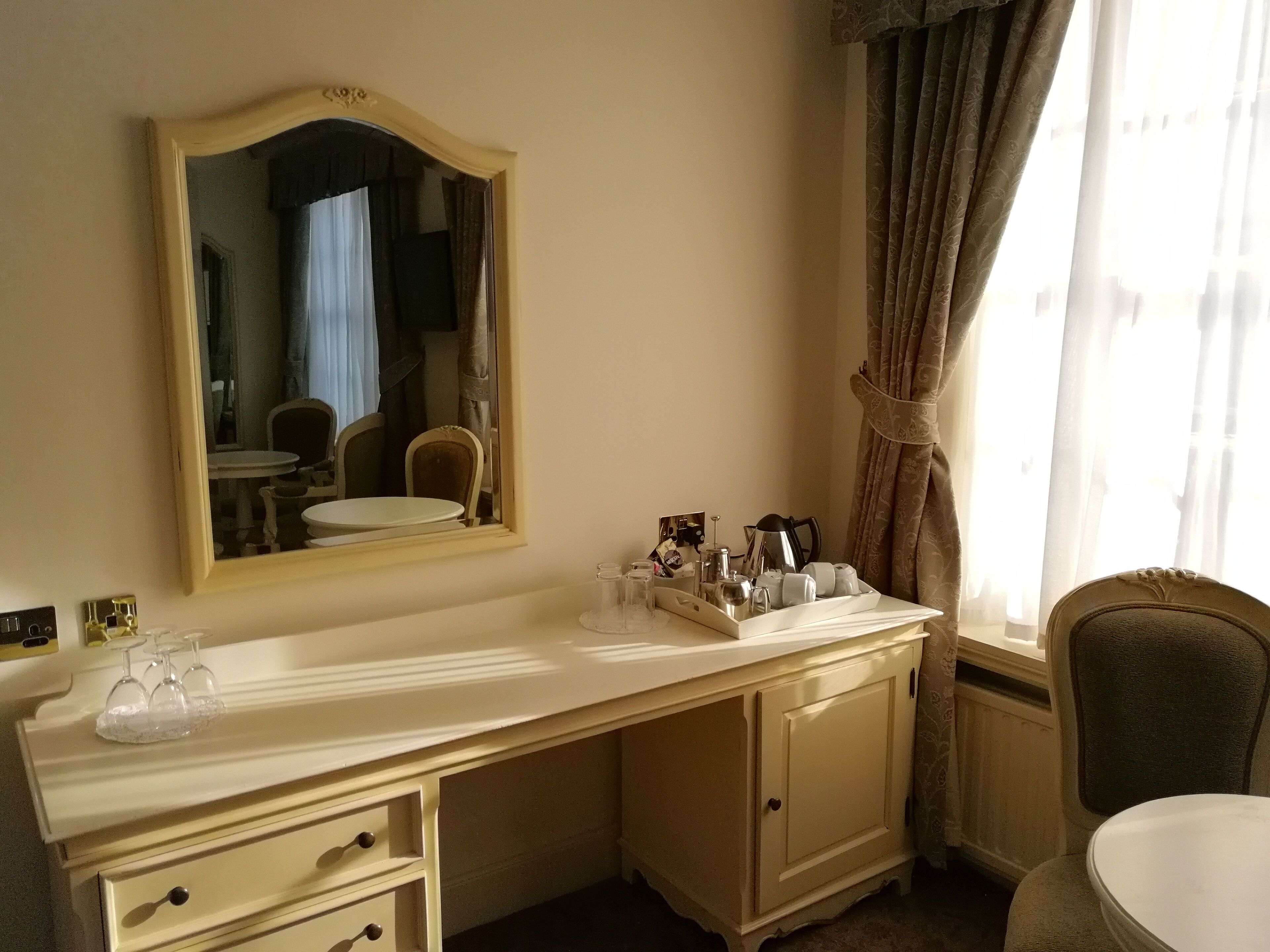 A hotel room with a large mirror, a vanity with a sink, a coffee maker, and a chair.