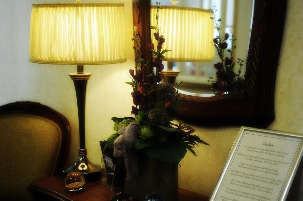 A lamp with a pleated shade, a vase with flowers, and a framed menu on a table.