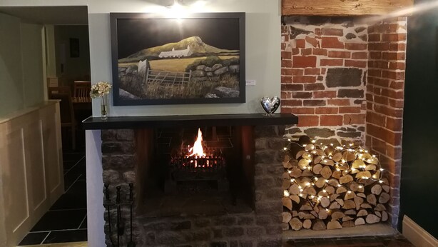 A fireplace with a TV mounted above it, a brick wall, and a stack of firewood with lights. - Feathers Hotel, Bar and Restaurant (Aberaeron)