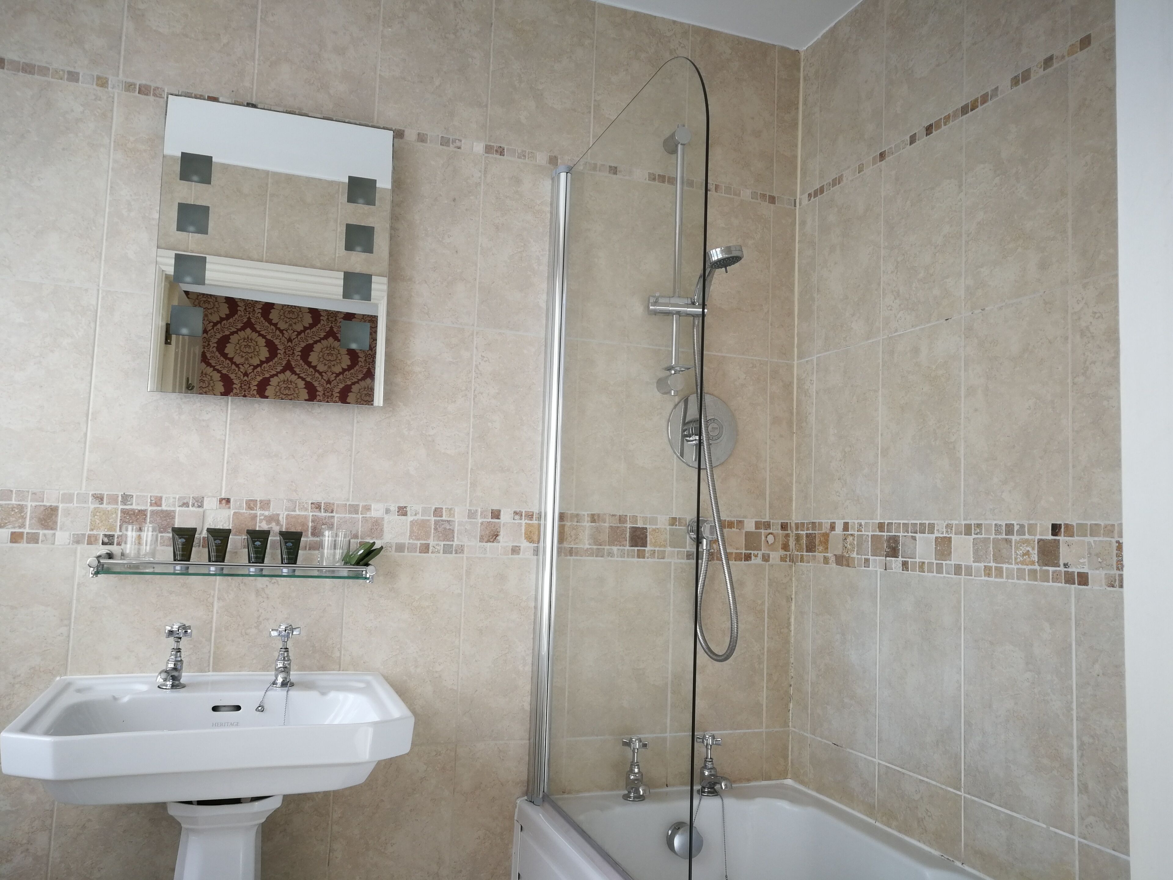 A bathroom with a sink, mirror, shower, and tiled walls.