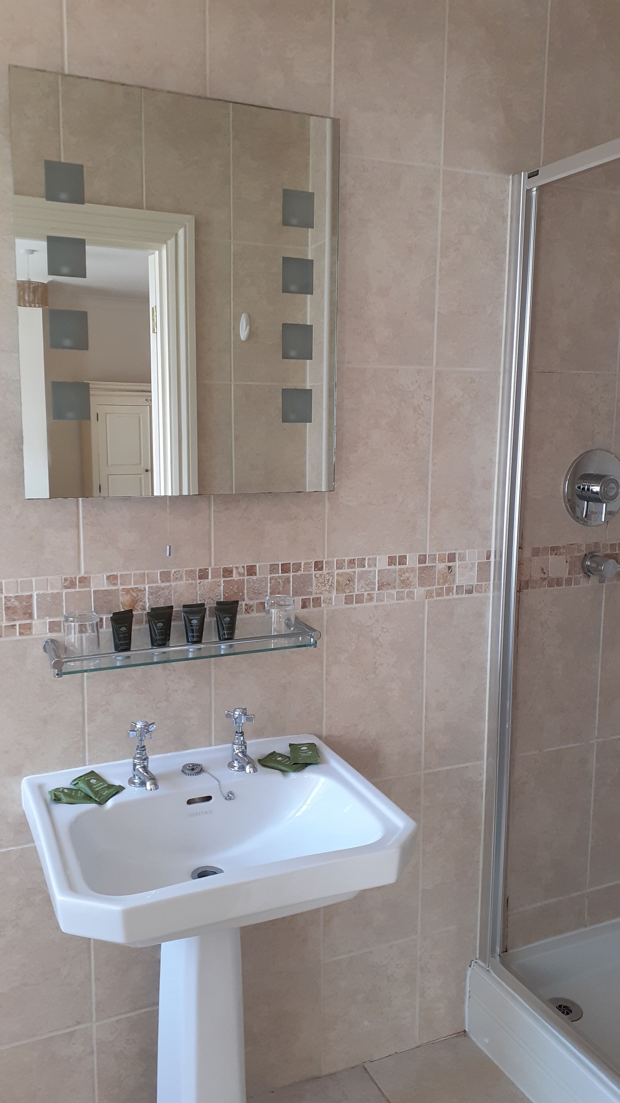 A bathroom with a white sink, two faucets, a mirror, and a shower area.