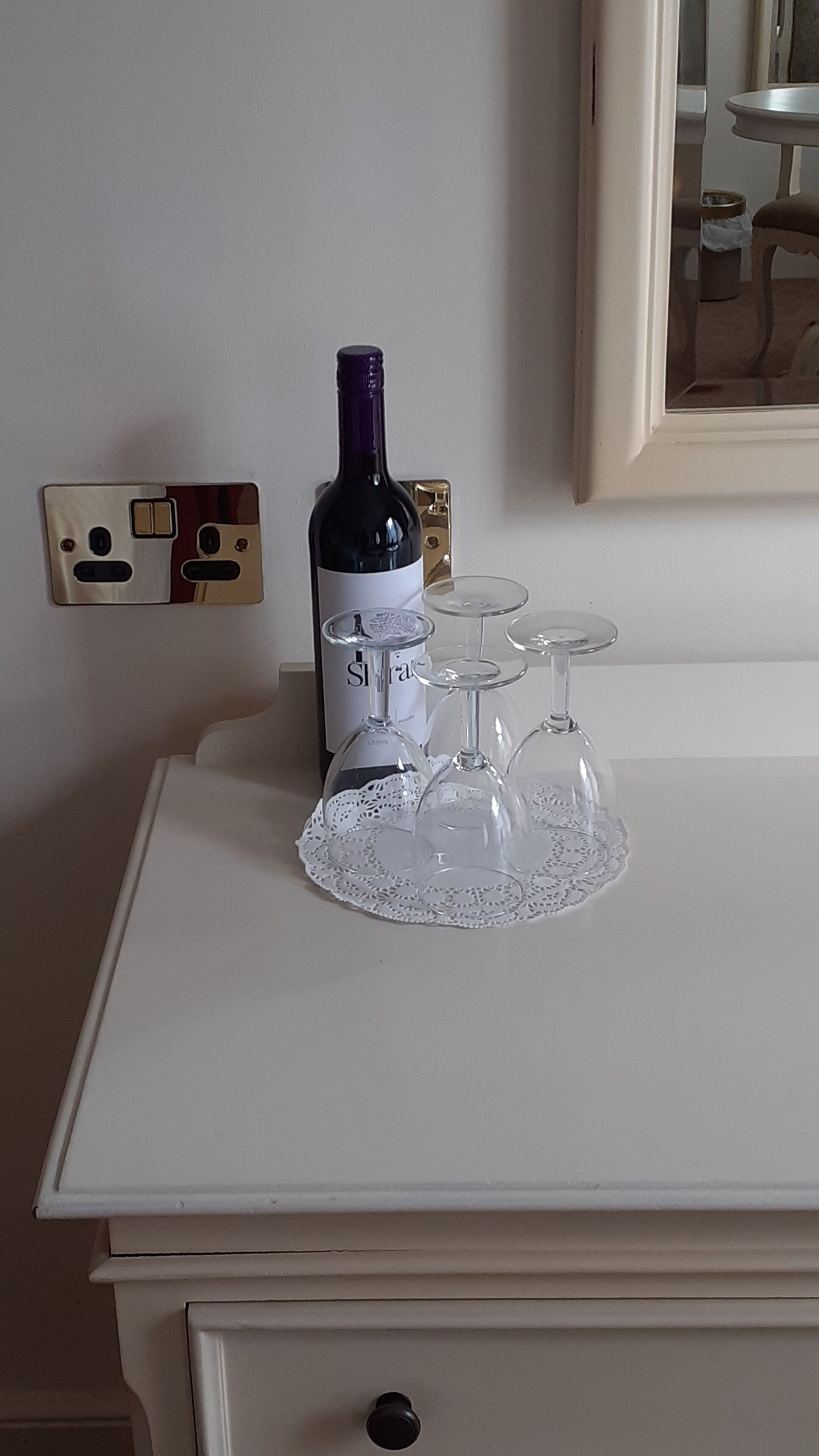 Un aparador blanco con una botella de vino y copas sobre él.