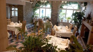 A restaurant with tables set for dining, stone walls, and large windows allowing natural light. - Feathers Hotel, Bar and Restaurant (Aberaeron)
