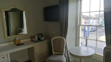 Habitación de hotel con escritorio, silla, una mesita, televisión y ventana con vista a la calle.