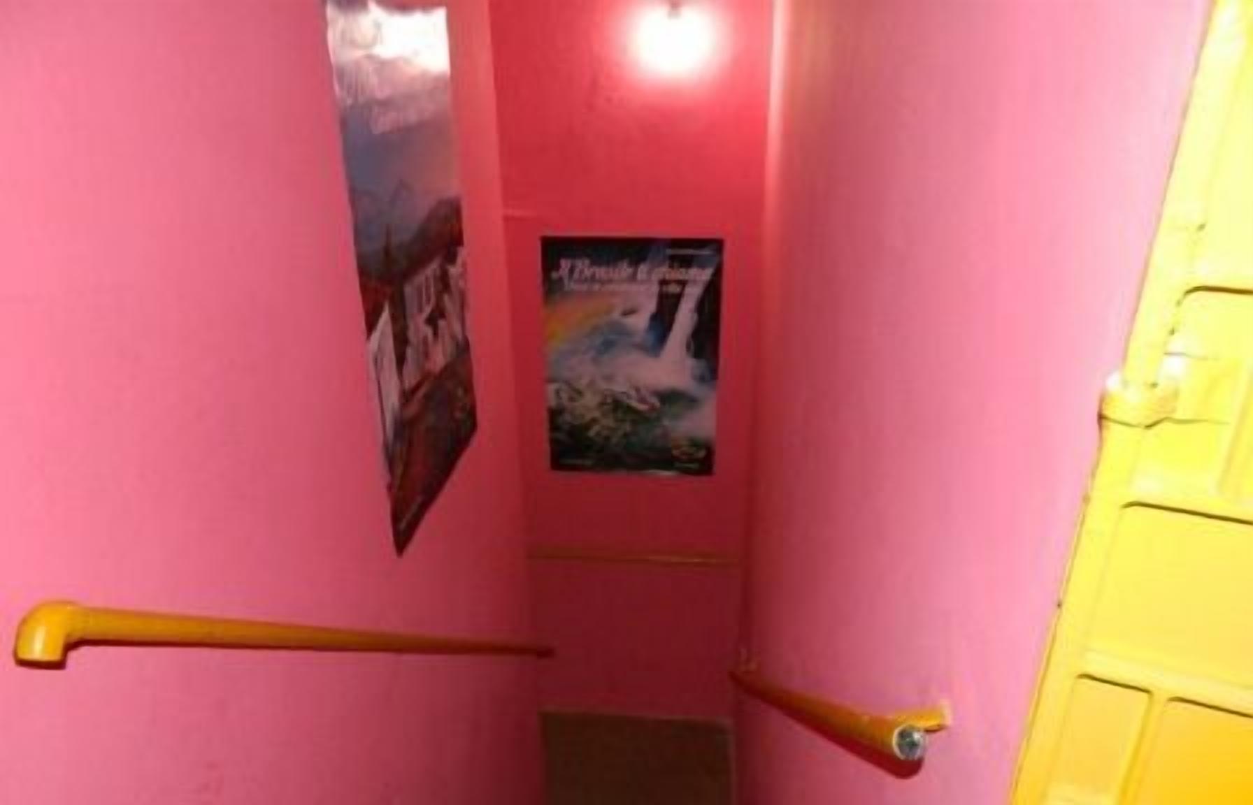A narrow hallway with pink walls, a yellow door, and a poster on the wall.