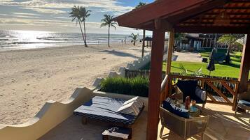 A beachside patio with a view of the ocean, palm trees, and a grassy area with outdoor furniture.