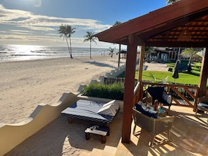 Un patio frente a la playa con vista al océano, palmeras y un espacio verde con mobiliario exterior.