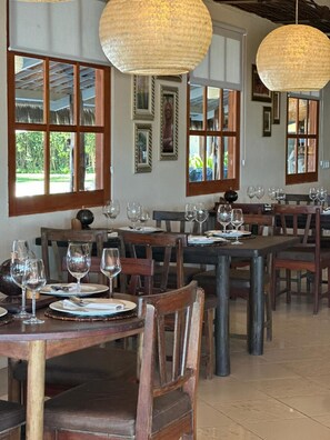 A restaurant interior with wooden tables and chairs, large woven pendant lights, and framed artwork on the walls. - Rede Beach (Trairi)