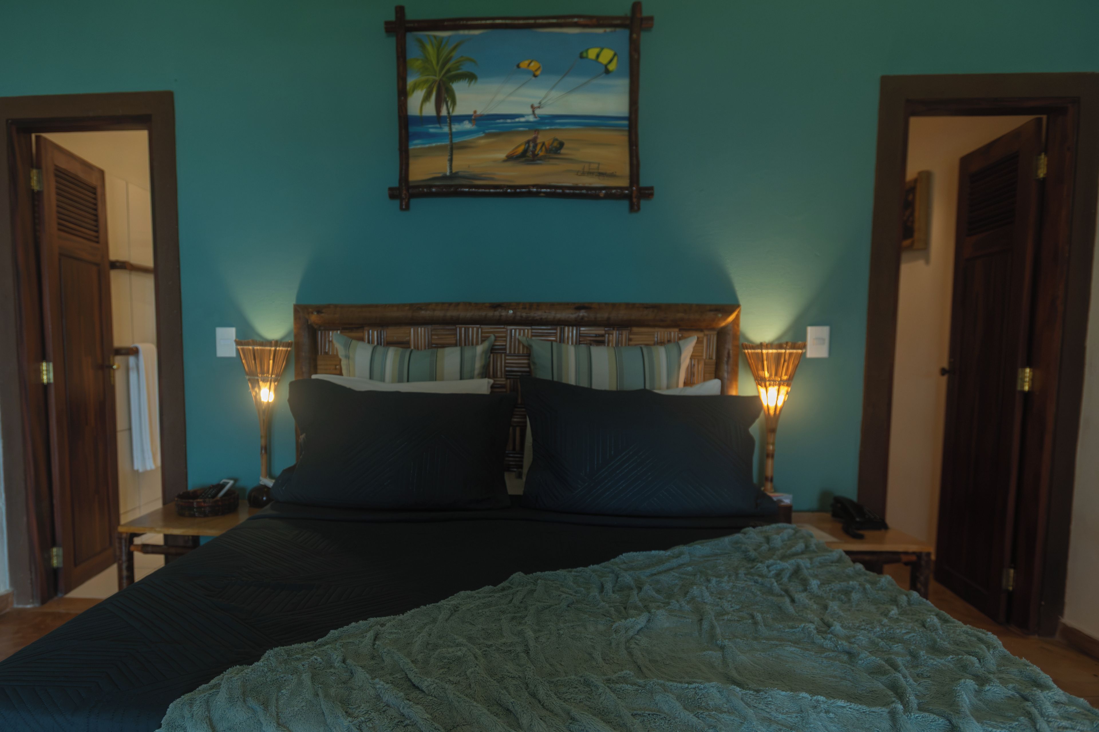 A bedroom with a bed, two bedside lamps, a nightstand, a painting of a beach scene, and a wooden headboard.