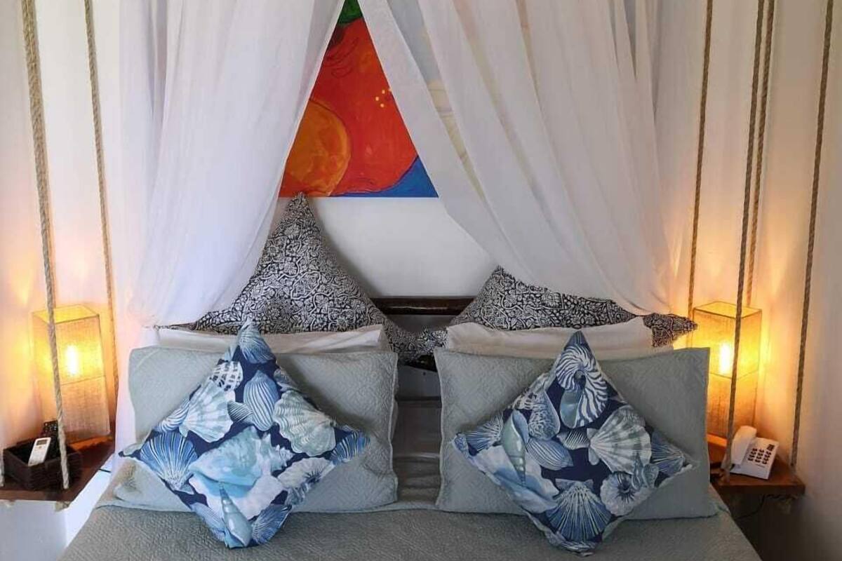 Uma cama com dossel, almofadas estampadas e um quadro colorido na parede.