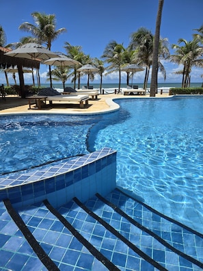 A swimming pool with tiled edges, lounge chairs, and palm trees.