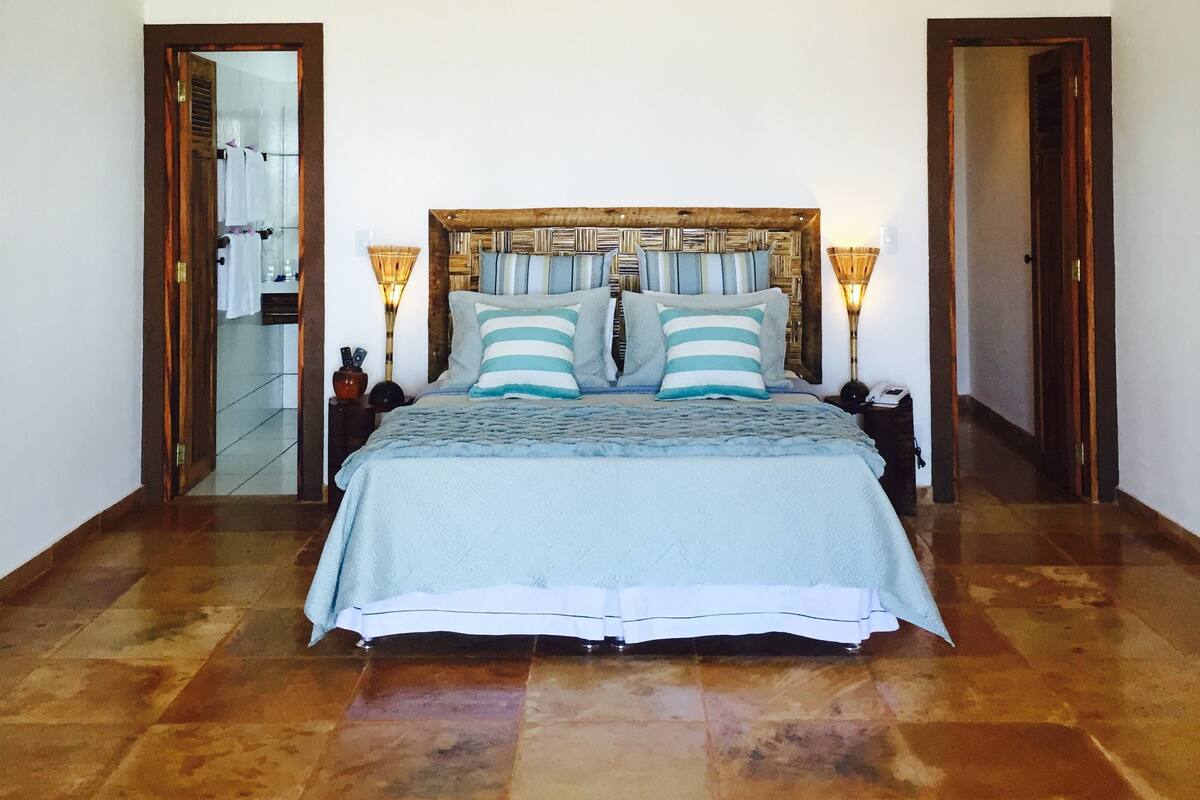 Quarto com uma cama grande, cabeceira de madeira, duas luminárias de apoio e um lustre.