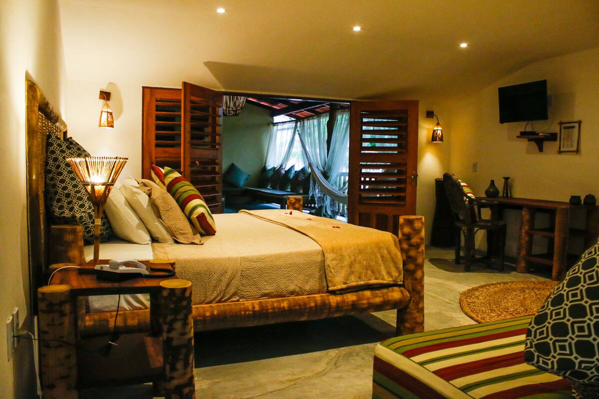 Quarto com uma cama grande, móveis de madeira, uma TV e uma escrivaninha.