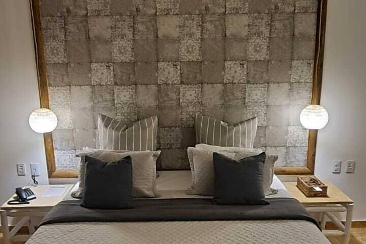 Quarto com uma cama grande, cabeceira estampada, duas mesas de cabeceira com luminárias e um lustre.