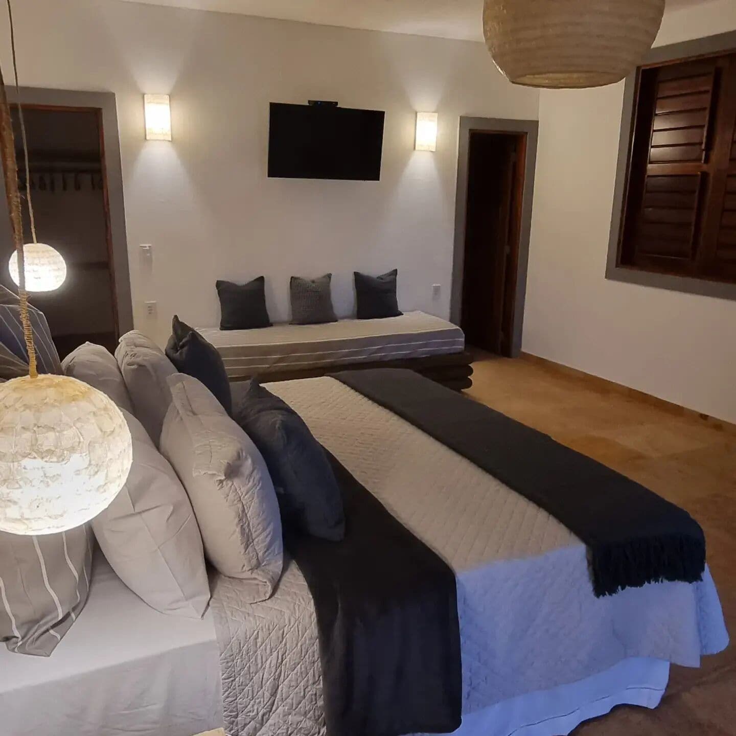 Un dormitorio con una cama, un sofá, un televisor montado en la pared y una lámpara colgante.
