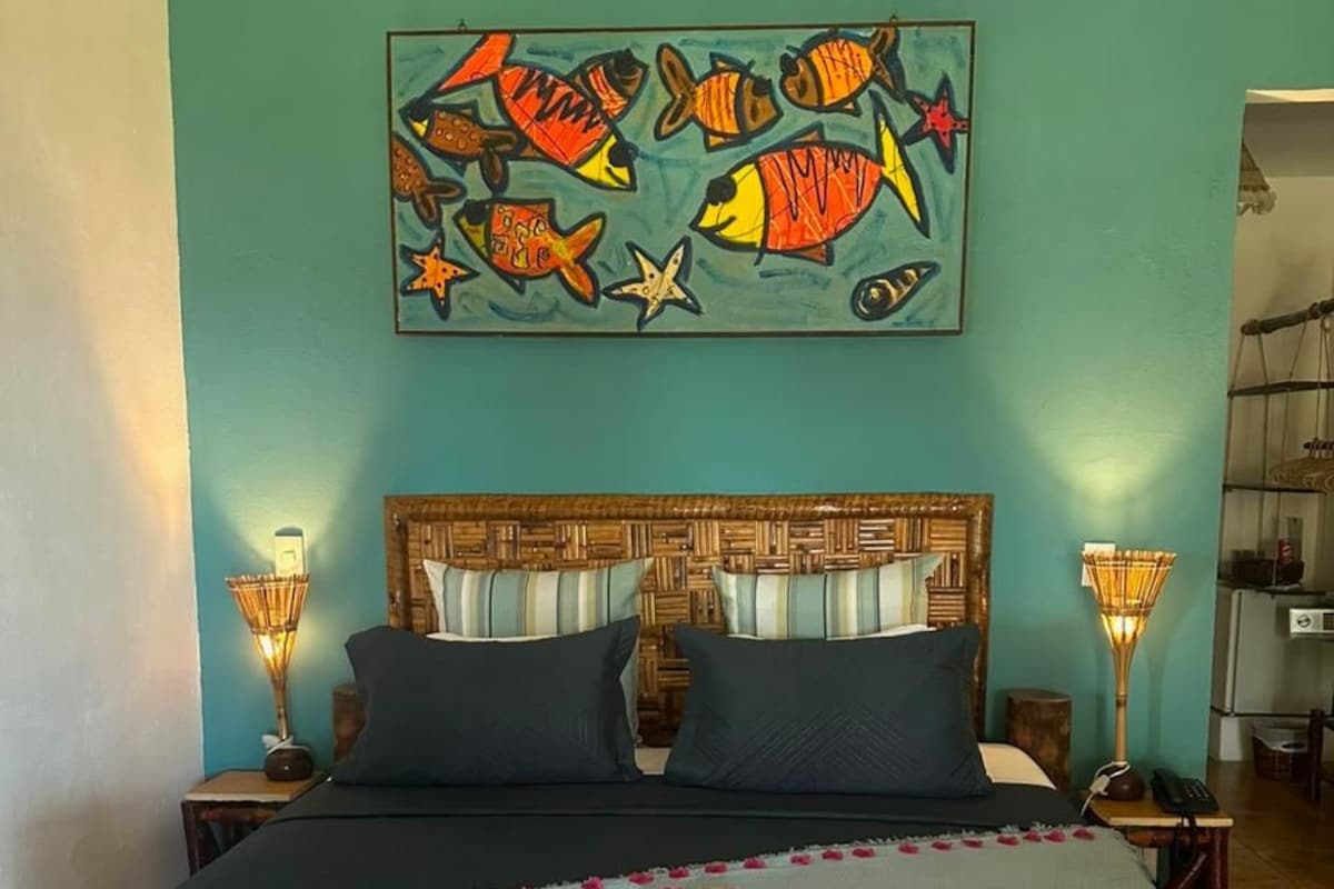 A double bed with a headboard, two bedside lamps, a framed artwork above the bed, and a bedside table with a lamp.