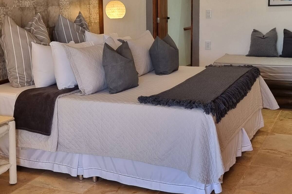 Quarto com uma cama grande, cabeceira com padrão texturizado, luminária pendente e um quadro na parede.