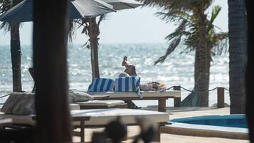 Uma área de lounge à beira-mar com espreguiçadeiras, piscina e vista para o oceano.