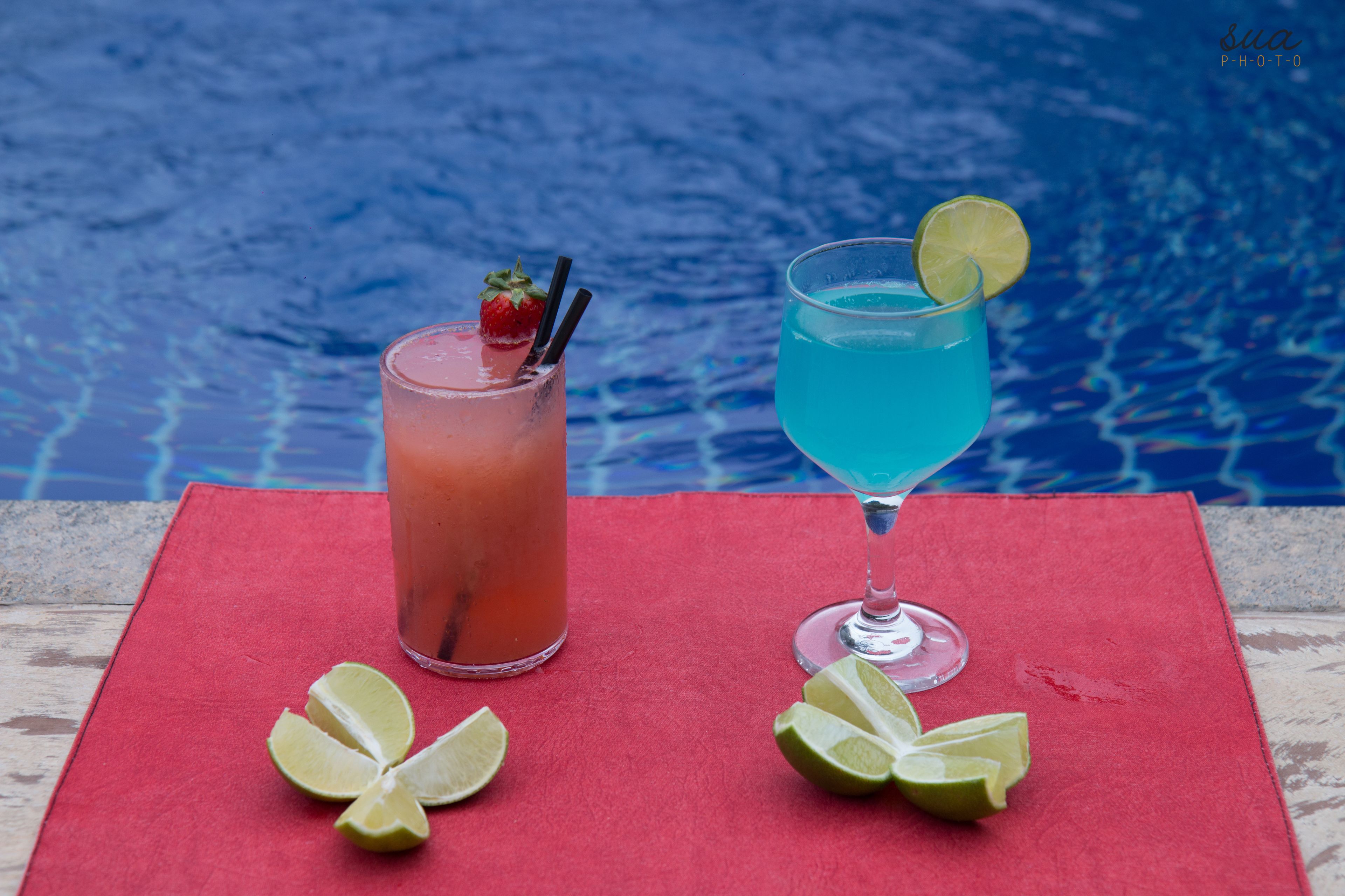 Dos bebidas con rodajas de lima sobre una alfombra roja junto a una piscina.