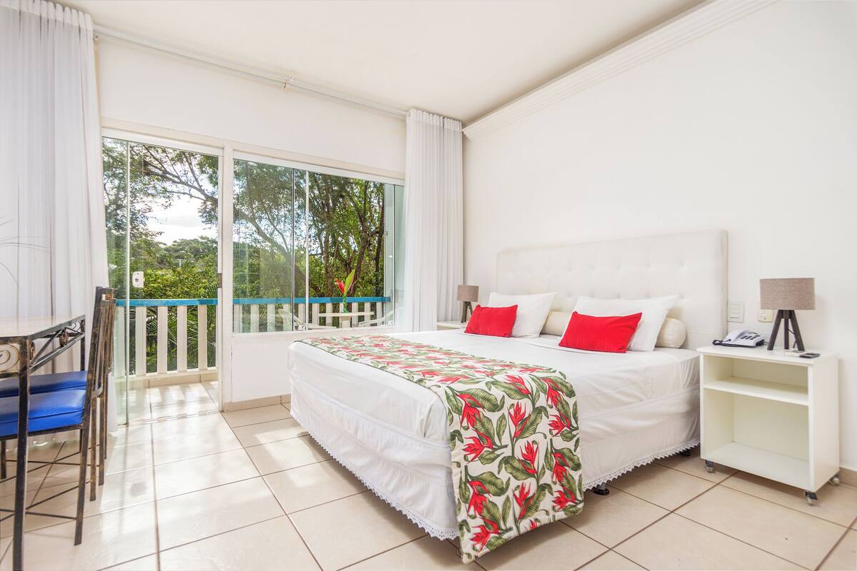Une chambre avec un grand lit, un balcon, un bureau et une table de chevet.