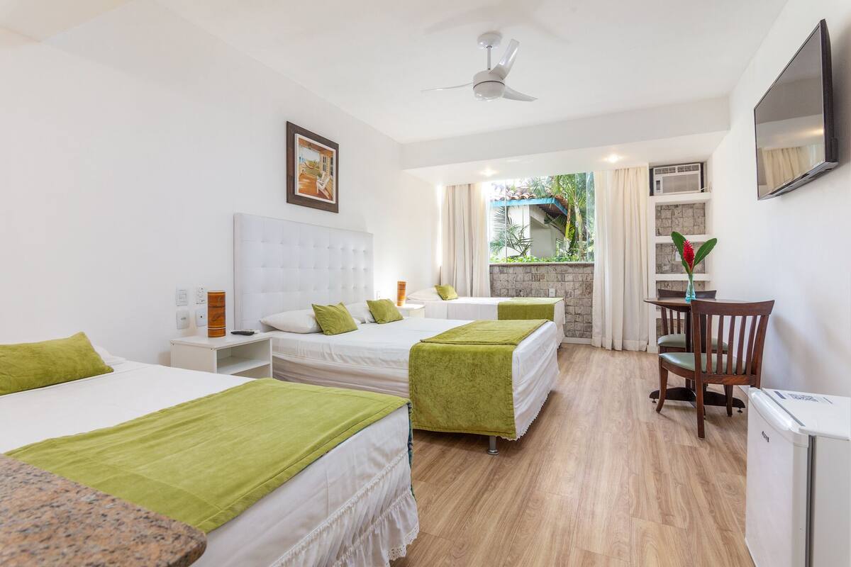 Une chambre d’hôtel avec trois lits, un bureau, une chaise, une télévision et un petit réfrigérateur.