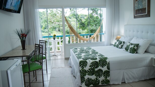 A bedroom with a bed, a TV, a dining table with chairs, and a view of the outdoors. - Hotel Miratlântico Búzios (Búzios)