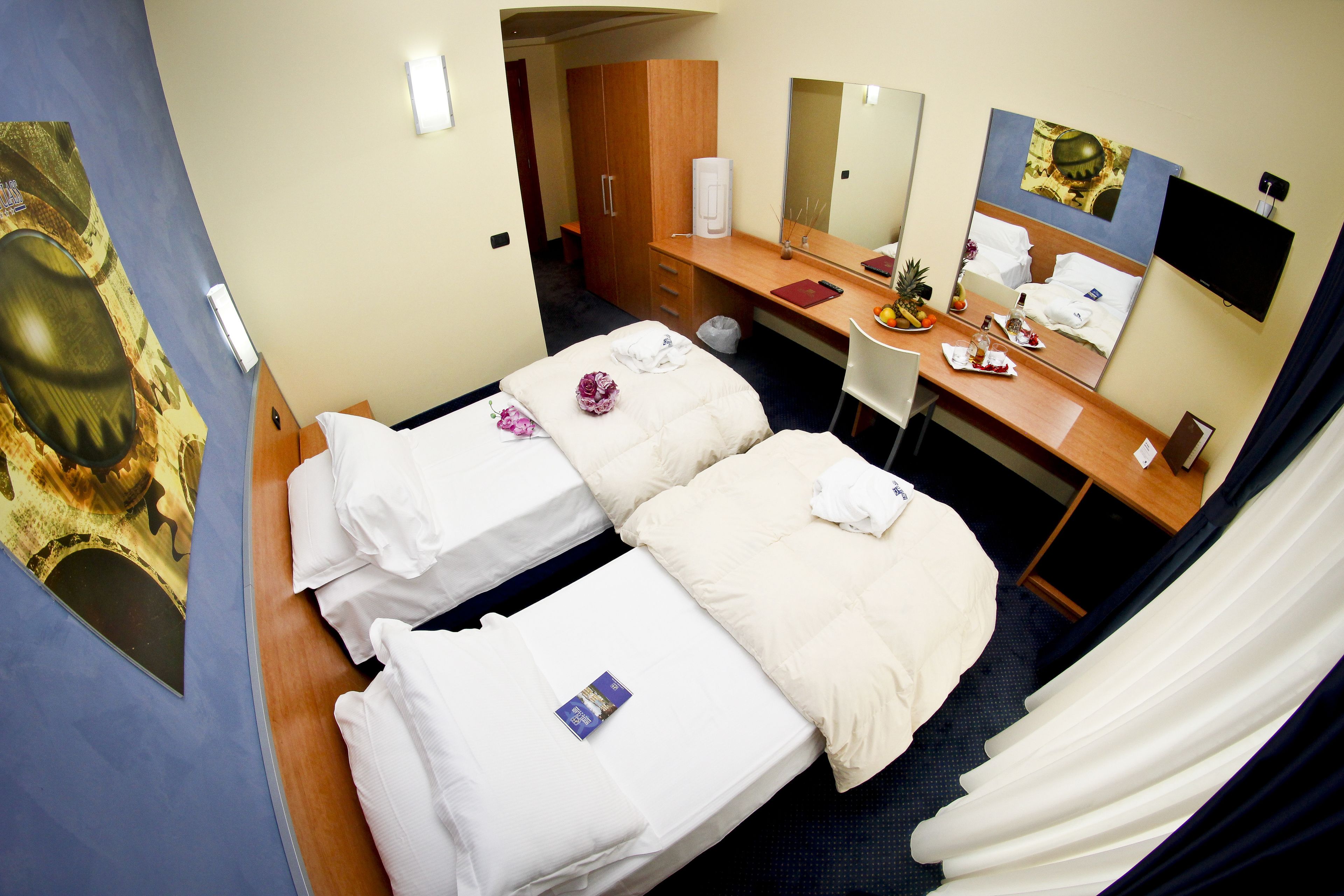 A hotel room with two beds, a desk, a mirror, a TV, and a bathroom.