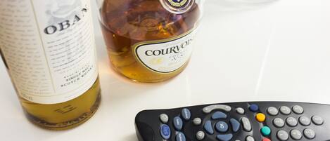A remote control, a bottle of Courvoisier cognac, and a bottle of Oban whisky on a white surface.
