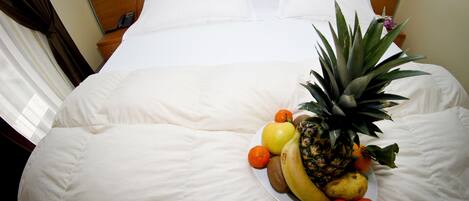 A neatly made bed with white linens, a fruit plate on the bed, and a wooden headboard.