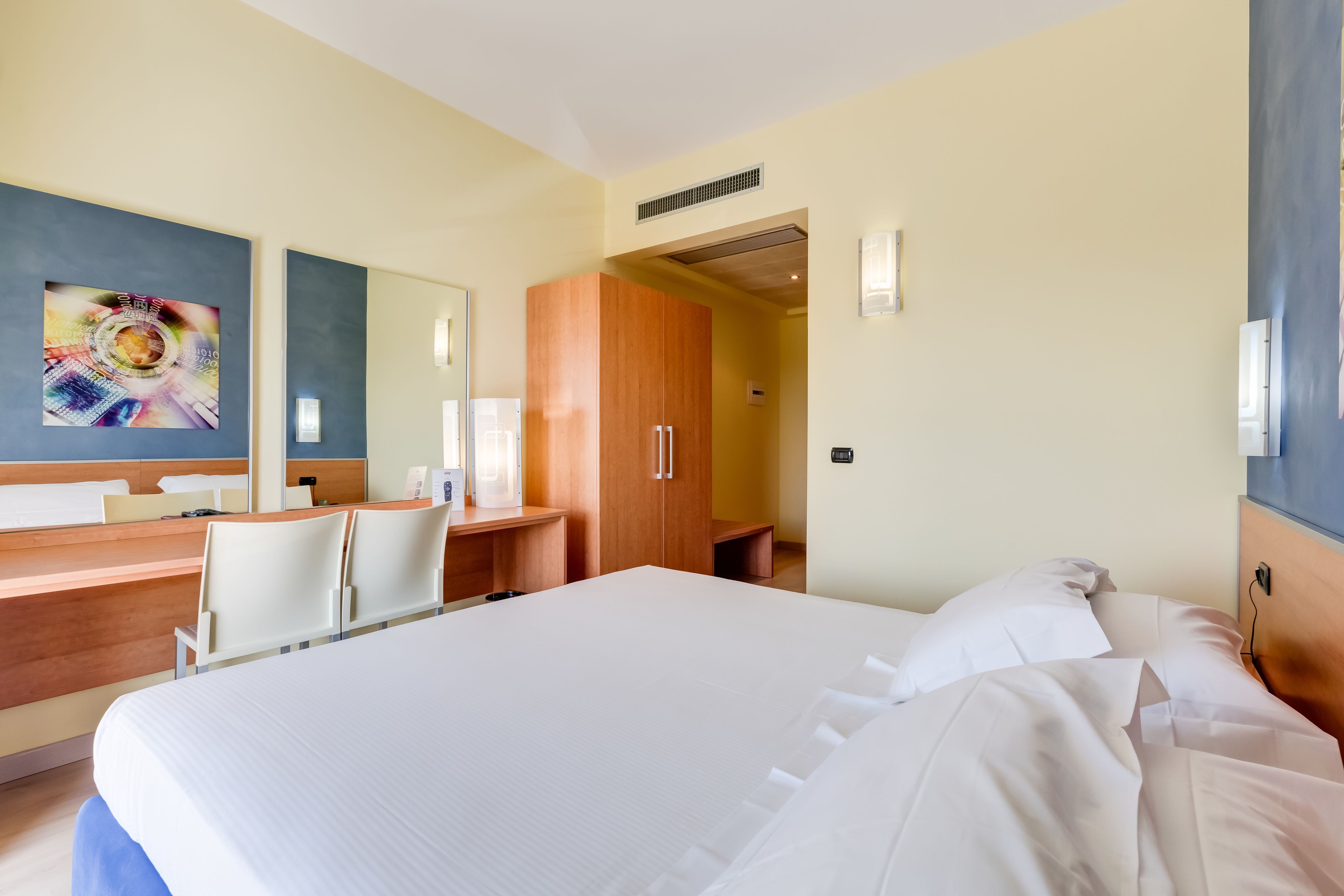 Habitación de hotel con una cama grande, un escritorio con sillas, un armario de madera y un espejo grande en la pared.